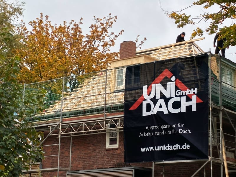 Eingerüstetes Wohnhaus mit offenem Dachstuhl und Bauschild der UNI DACH GmbH während der Dachsanierung