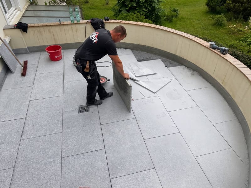 Mitarbeiter der UNI DACH GmbH schneidet eine Granitplatte beim Verlegen auf einer runden Terrasse